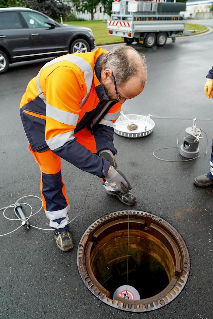Kommunaker Mitarbeiter lässt Köderbox in den Kanal ab.